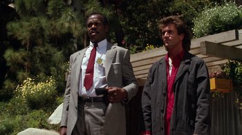 Movie still from “Lethal Weapon” (1987), directed by Richard Donner – Two men standing next to each other wearing suits and ties; Medium shot, Low angle