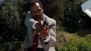 Movie still from “Lethal Weapon” (1987), directed by Richard Donner – A man in a suit and tie holding a gun in his hand; Close Up shot, Low angle