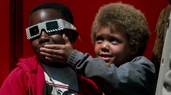 Movie still from “Lethal Weapon” (1987), directed by Richard Donner – Two children wearing solar eclipse glasses and one is holding his hand up to his face; Close Up shot, Over the shoulder angle