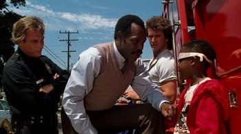 Movie still from “Lethal Weapon” (1987), directed by Richard Donner – A man in a vest and tie leaning on another man's leg; Medium shot, Over the shoulder angle