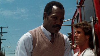 Movie still from “Lethal Weapon” (1987), directed by Richard Donner – A man in a vest and tie standing next to another man; Close Up shot, Low angle