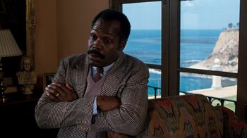 Movie still from “Lethal Weapon” (1987), directed by Richard Donner – A man sitting on a couch in front of a window; Close Up shot, Over the shoulder angle