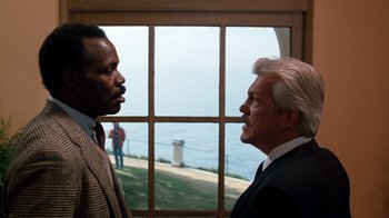 Movie still from “Lethal Weapon” (1987), directed by Richard Donner – Two men standing next to each other in front of a window; Medium shot, Over the shoulder angle