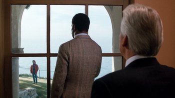 Movie still from “Lethal Weapon” (1987), directed by Richard Donner – Two men in suits looking out of a window; Extreme Wide shot, Over the shoulder angle