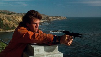 Movie still from “Lethal Weapon” (1987), directed by Richard Donner – A man in an orange jacket is holding a gun; Medium shot, Low angle