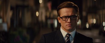Movie still from “Kingsman: The Golden Circle” (2017), directed by Matthew Vaughn – A person wearing a suit and glasses; Close Up shot, Over the shoulder angle