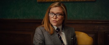 Movie still from “Kingsman: The Golden Circle” (2017), directed by Matthew Vaughn – A woman wearing a suit and tie with glasses; Medium shot, Over the shoulder angle