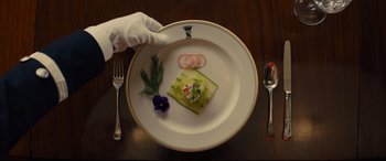 Movie still from “Kingsman: The Golden Circle” (2017), directed by Matthew Vaughn – A white plate topped with food on top of a wooden table; Extreme Close Up shot, Overhead angle
