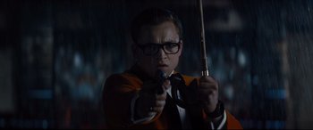 Movie still from “Kingsman: The Golden Circle” (2017), directed by Matthew Vaughn – A man holding a gun while wearing glasses; Close Up shot, Low angle