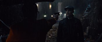 Movie still from “Kingsman: The Golden Circle” (2017), directed by Matthew Vaughn – A man holding a gun pointed at another man in the rain with an umbrella; Medium shot, Over the shoulder angle