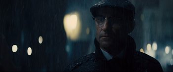 Movie still from “Kingsman: The Golden Circle” (2017), directed by Matthew Vaughn – A man wearing glasses and a hat standing in the rain; Close Up shot, Over the shoulder angle