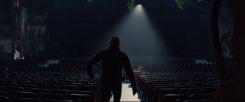Movie still from “Kingsman: The Golden Circle” (2017), directed by Matthew Vaughn – A man standing in a dark room with rows of seats; Extreme Wide shot, Low angle