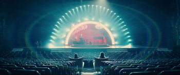 Movie still from “Kingsman: The Golden Circle” (2017), directed by Matthew Vaughn – Two people sitting in seats in front of a stage; Extreme Wide shot, High angle