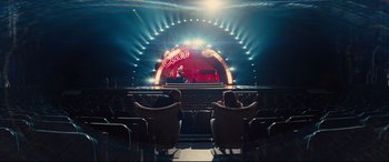 Movie still from “Kingsman: The Golden Circle” (2017), directed by Matthew Vaughn – Two people sitting in chairs in front of a stage; Extreme Wide shot, High angle