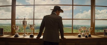 Movie still from “Kingsman: The Golden Circle” (2017), directed by Matthew Vaughn – A man standing in front of a window with a cowboy hat on; Wide shot, Low angle