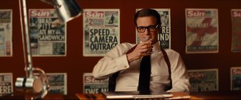 Movie still from “Kingsman: The Golden Circle” (2017), directed by Matthew Vaughn – A man sitting at a table drinking a glass of water; Medium shot, Over the shoulder angle