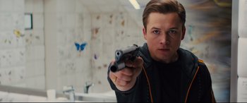 Movie still from “Kingsman: The Golden Circle” (2017), directed by Matthew Vaughn – A man holding a gun in a room with a butterfly on the wall behind him; Close Up shot, Low angle