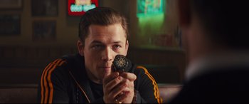 Movie still from “Kingsman: The Golden Circle” (2017), directed by Matthew Vaughn – A man is holding a doughnut in his hand; Close Up shot, Over the shoulder angle