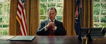 Movie still from “Kingsman: The Golden Circle” (2017), directed by Matthew Vaughn – A man sitting at a table in front of a window; Medium shot, Low angle