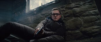 Movie still from “Kingsman: The Golden Circle” (2017), directed by Matthew Vaughn – A man sitting on the ground holding a cell phone; Medium shot, High angle