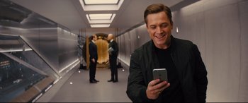 Movie still from “Kingsman: The Golden Circle” (2017), directed by Matthew Vaughn – A man smiling while looking at his phone; Medium shot, Over the shoulder angle