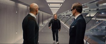 Movie still from “Kingsman: The Golden Circle” (2017), directed by Matthew Vaughn – A man walking down a hallway with two other men; Wide shot, Over the shoulder angle