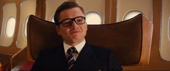 Movie still from “Kingsman: The Golden Circle” (2017), directed by Matthew Vaughn – A man wearing a suit and tie sitting in a chair; Close Up shot, Low angle