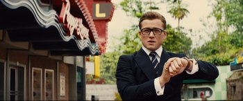 Movie still from “Kingsman: The Golden Circle” (2017), directed by Matthew Vaughn – A man in a suit and tie holding a cigarette; Medium shot, Low angle