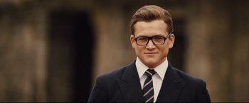 Movie still from “Kingsman: The Golden Circle” (2017), directed by Matthew Vaughn – A man in a suit and tie wearing glasses; Close Up shot, Over the shoulder angle