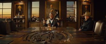 Movie still from “Kingsman: The Golden Circle” (2017), directed by Matthew Vaughn – A man sitting at a table holding a glass of beer; Wide shot, Over the shoulder angle