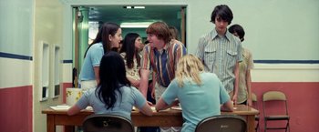 Movie still from “Licorice Pizza” (2021), directed by Paul Thomas Anderson – A group of people sitting at a table talking to each other; Medium shot, Over the shoulder angle