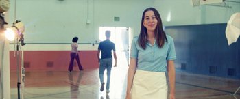 Movie still from “Licorice Pizza” (2021), directed by Paul Thomas Anderson – A woman standing in front of two other people in a room; Medium shot, Low angle