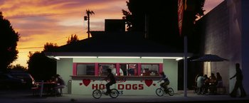 Movie still from “Licorice Pizza” (2021), directed by Paul Thomas Anderson – Two people riding bikes in front of an ice cream shop; Extreme Wide shot, Low angle