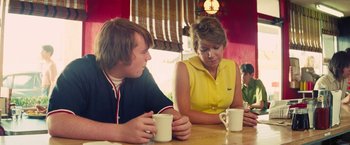 Movie still from “Licorice Pizza” (2021), directed by Paul Thomas Anderson – A woman and a boy sitting at a table with cups of coffee; Medium shot, Over the shoulder angle