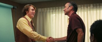 Movie still from “Licorice Pizza” (2021), directed by Paul Thomas Anderson – A man and a boy shaking hands in front of a window; Medium shot, Over the shoulder angle