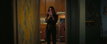Movie still from “Licorice Pizza” (2021), directed by Paul Thomas Anderson – A woman standing in a kitchen talking on a phone; Medium shot, High angle