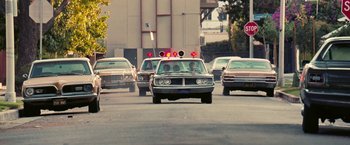 Movie still from “Licorice Pizza” (2021), directed by Paul Thomas Anderson – A group of cars driving down a street; Wide shot, Low angle