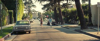 Movie still from “Licorice Pizza” (2021), directed by Paul Thomas Anderson – A man and a woman running down a street; Wide shot, High angle