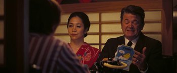 Movie still from “Licorice Pizza” (2021), directed by Paul Thomas Anderson – A woman in a red dress sitting at a table; Medium shot, Over the shoulder angle