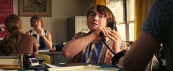 Movie still from “Licorice Pizza” (2021), directed by Paul Thomas Anderson – A man sitting at a table talking on a phone; Medium shot, Over the shoulder angle