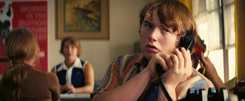 Movie still from “Licorice Pizza” (2021), directed by Paul Thomas Anderson – A man sitting in front of a woman holding a phone to his ear; Close Up shot, Over the shoulder angle