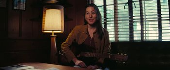 Movie still from “Licorice Pizza” (2021), directed by Paul Thomas Anderson – A woman sitting at a table with a guitar in front of a window; Medium shot, High angle