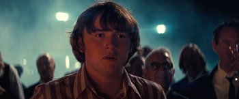 Movie still from “Licorice Pizza” (2021), directed by Paul Thomas Anderson – A young man with long brown hair wearing a striped shirt; Close Up shot, Low angle