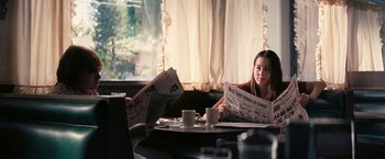 Movie still from “Licorice Pizza” (2021), directed by Paul Thomas Anderson – A woman sitting at a table reading a newspaper; Medium shot, Over the shoulder angle