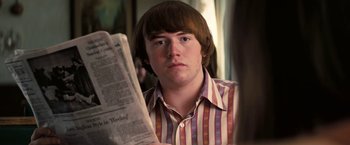 Movie still from “Licorice Pizza” (2021), directed by Paul Thomas Anderson – A young man reading a newspaper while sitting in a chair; Close Up shot, Over the shoulder angle