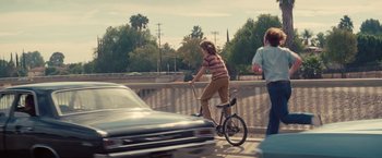 Movie still from “Licorice Pizza” (2021), directed by Paul Thomas Anderson – A person riding a bike on a bridge next to cars; Wide shot, High angle