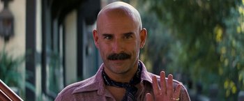Movie still from “Licorice Pizza” (2021), directed by Paul Thomas Anderson – A bald man with a mustache is waving to the camera; Close Up shot, Low angle
