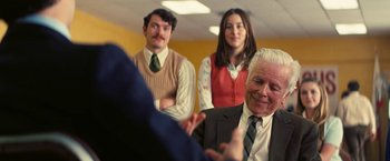 Movie still from “Licorice Pizza” (2021), directed by Paul Thomas Anderson – A group of people in a room with a man in a suit; Medium shot, Over the shoulder angle