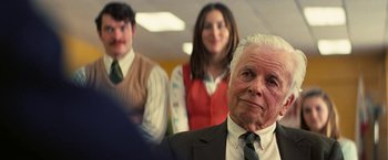 Movie still from “Licorice Pizza” (2021), directed by Paul Thomas Anderson – An older man in a suit and tie with two other people in the background; Close Up shot, Over the shoulder angle