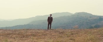 Movie still from “Licorice Pizza” (2021), directed by Paul Thomas Anderson – A man standing on top of a dry grass field; Extreme Wide shot, Low angle